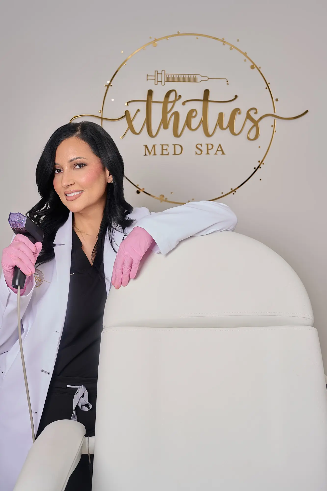 Leticia Camacho, PA-C, standing in front of the gold Xthetics Med Spa logo while holding a medical aesthetics device.